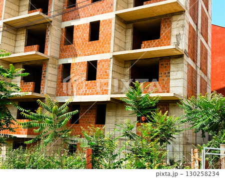 Unfinished apartment building with exposed brick walls. Urban development, civil engineering, and residential construction in progress. Unfinished apartment building with exposed brick walls. Urban development, civil engineering, and residential construction in progress. 130258234