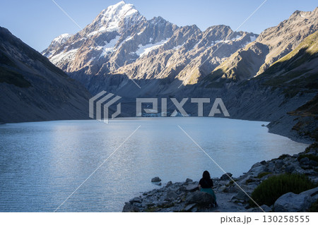 Woman sitting on a bank of glacial lake looking at a glaciers and mountain, Mt Cook, New Zealand 130258555