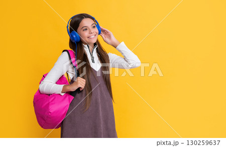 glad child in headphones with school backpack on yellow background glad child in headphones with school backpack on yellow background 130259637
