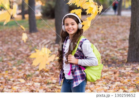 kid in autumn park. happy kid walk among autumn leaves. small girl wear headphones. back to school. modern education. child with school backpack in fall forest. concept of knowledge day 130259652