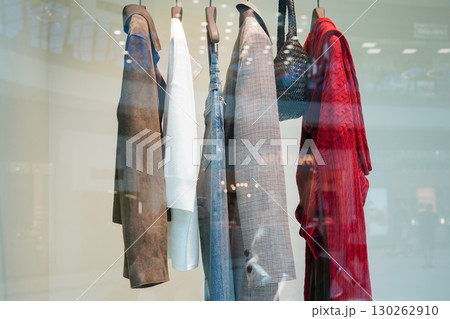 A row of stylish clothes and accessories hanging in a modern store display behind glass A row of stylish clothes and accessories hanging in a modern store display behind glass 130262910