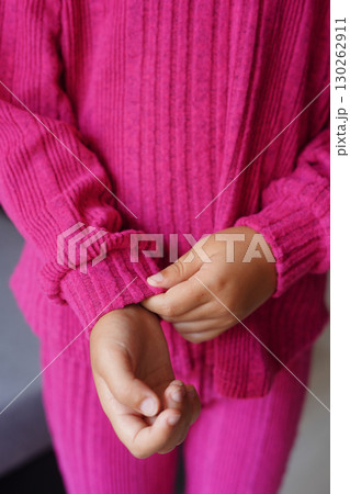A close-up of a child wearing a vibrant pink ribbed knit outfit with hands adjusting the sleeve 130262911