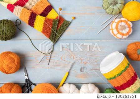 Cozy composition for needlework from basket with balls for knitting warm clothes, striped fabric for future scarf and knitted pumpkin toys on table with knitting needles, crochet hooks and scissors. Cozy composition for needlework from basket with balls for knitting warm clothes, striped fabric for future scarf and knitted pumpkin toys on table with knitting needles, crochet hooks and scissors. 130263251