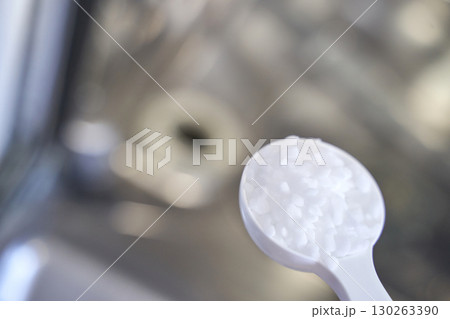 Close up of white dishwasher detergent powder on a spoon near a stainless steel 130263390