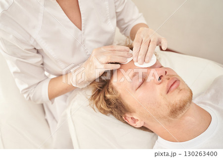 Young caucasian male receiving skincare treatment from professional in white Young caucasian male receiving skincare treatment from professional in white 130263400