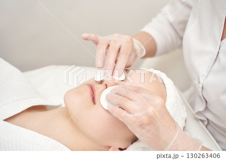 Caucasian female receiving facial treatment with cotton pads and gloves in spa Caucasian female receiving facial treatment with cotton pads and gloves in spa 130263406