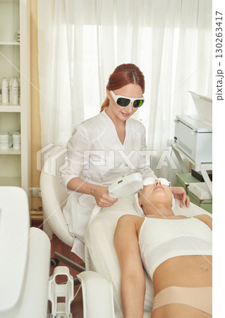 Young caucasian female receiving laser facial treatment in modern aesthetic Young caucasian female receiving laser facial treatment in modern aesthetic 130263417