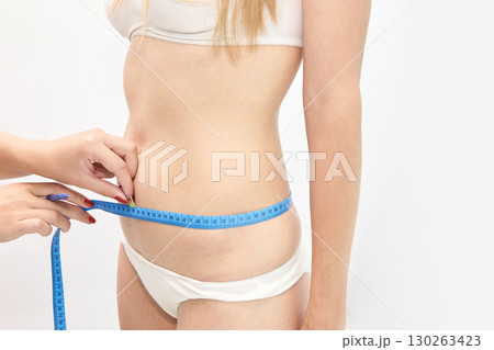 Caucasian young female waist measurement with blue tape for health and fitness 130263423