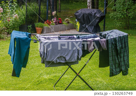 Freshly washed clothes hanging on a drying rack outside in a backyard garden on a sunny day, symbolizing home chores, eco-friendly lifestyle, and cleanliness. High quality photo 130263749