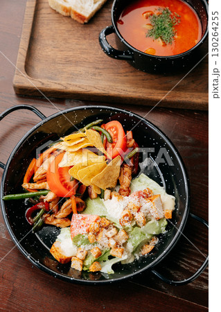 Top view of hearty lunch with tomato soup, salad, grilled chicken and nachos on rustic table 130264255
