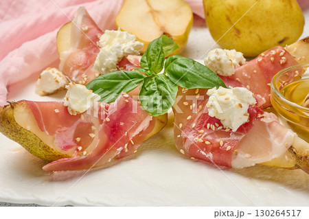 Pear slice wrapped in prosciutto with cheese and sesame seeds on a white board Pear slice wrapped in prosciutto with cheese and sesame seeds on a white board 130264517