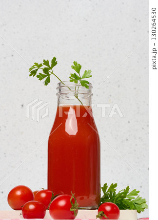 Glass bottle with tomato juice decorated with parsley. Nearby are fresh red tomatoes and parsley leaves on a light background. 130264530