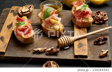 Italian bruschetta with prosciutto, pear slices, cream cheese and fresh basil, garnished with sesame seeds, served on a rustic wooden board 130264562