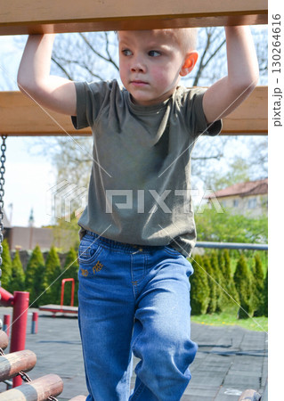 A child climbs up an alpine grid in a park on a playground on a hot summer day. children's playground in a public park, entertainment and recreation for children, mountaineering training. High quality 130264616