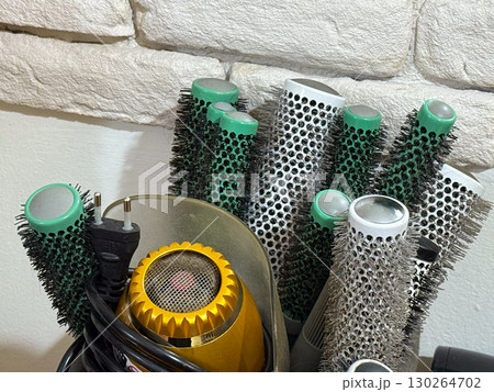 Collection of round hair brushes and a yellow hair dryer in a salon. Hairstyling, professional tools, and beauty care equipment. Collection of round hair brushes and a yellow hair dryer in a salon. Hairstyling, professional tools, and beauty care equipment. 130264702