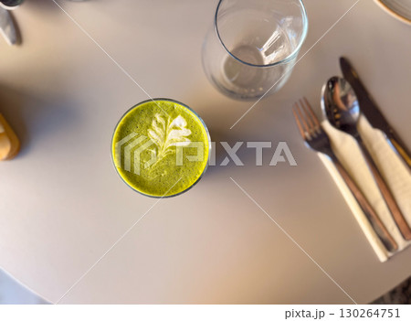 Glass of matcha latte with leaf foam art served on cafe table in soft daylight top view. Healthy beverage, Japanese tea culture, and modern wellness lifestyle Glass of matcha latte with leaf foam art served on cafe table in soft daylight top view. Healthy beverage, Japanese tea culture, and modern wellness lifestyle 130264751