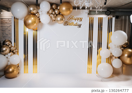 Elegant birthday photo zone with white and gold balloon decor and festive backdrop 130264777