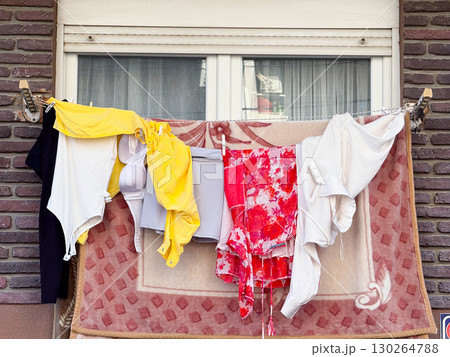 Laundry hanging on balcony rope with colorful clothes and textiles against brick wall. Domestic lifestyle, everyday urban culture, and household routine in residence. 130264788