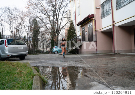 Woman walking through a parking lot after rain, reflecting puddles along the path in a quiet neighborhood setting during early evening hours 130264911
