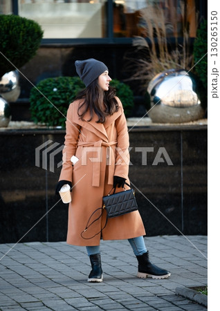 Fashionable woman enjoying a warm drink while standing alone against a stylish urban landscape on a crisp autumn day 130265150