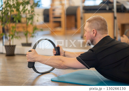 Male fitness Pilates trainer shows exercises on special simulators. Rubber rings for stretching. High quality photo Male fitness Pilates trainer shows exercises on special simulators. Rubber rings for stretching. High quality photo 130266130