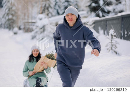 Smiling man giving sledding ride to woman. Love and leisure concept. High quality photo 130266219