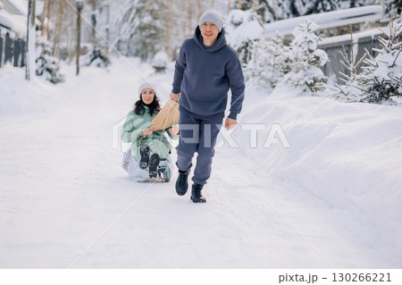 Smiling man giving sledding ride to woman. Love and leisure concept. High quality photo 130266221