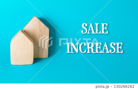 Two wooden houses are on a blue background with the words "Sale Increase" writte Two wooden houses are on a blue background with the words "Sale Increase" writte 130266262