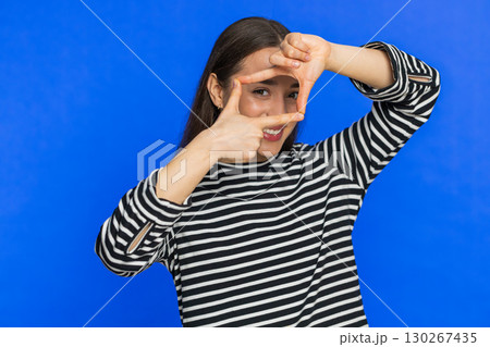 Woman photographer gesturing picture frame with hands, looks through fingers focusing cropping image 130267435