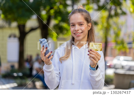 Happy young woman using credit bank card and smartphone purchases online shopping on city street Happy young woman using credit bank card and smartphone purchases online shopping on city street 130267437