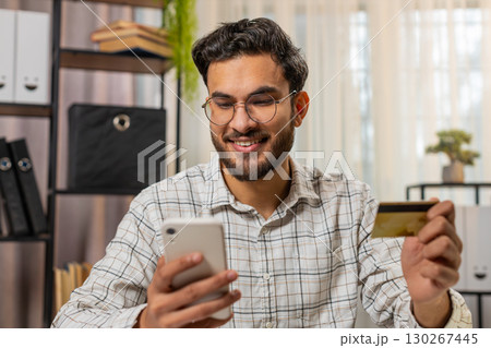 Happy Indian businessman using bank credit card and smartphone for online shopping bill payments Happy Indian businessman using bank credit card and smartphone for online shopping bill payments 130267445