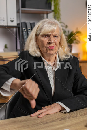 Upset senior businesswoman girl showing thumb down gesture expressing bad work at home office table Upset senior businesswoman girl showing thumb down gesture expressing bad work at home office table 130267587