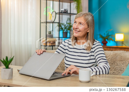 Mature woman happily closing laptop after completing important task, smiling and relaxing at table Mature woman happily closing laptop after completing important task, smiling and relaxing at table 130267588