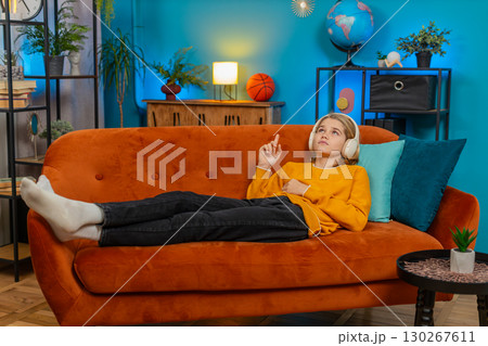 Teenager boy listening to audiobook with wireless headphones lying on sofa learning language at home Teenager boy listening to audiobook with wireless headphones lying on sofa learning language at home 130267611