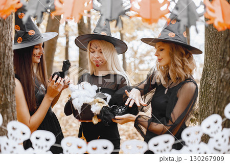 Three young girls witches in forest on Halloween. Girls wearing in black dresses and cone hat. Witches holding a magician stuff. 130267909