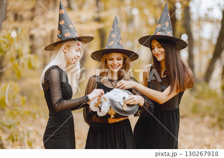 Three young girls witches in forest on Halloween. Girls wearing black dresses and cone hat. Witch holding a magician cauldron. Three young girls witches in forest on Halloween. Girls wearing black dresses and cone hat. Witch holding a magician cauldron. 130267918