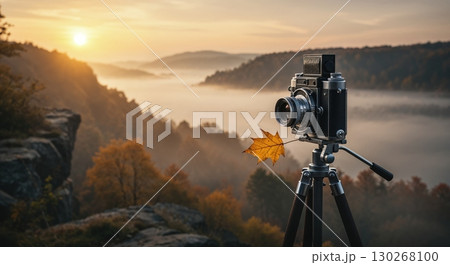 A vintage camera on a tripod captures a stunning autumn sunrise over a misty valley with colorful foliage and rolling hills. 130268100
