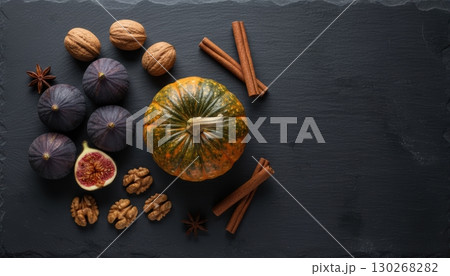 A top-down flat lay showcases a vibrant small pumpkin, purple figs, walnuts, cinnamon sticks, and star anise arranged on a dark slate background with ample copy space. A top-down flat lay showcases a vibrant small pumpkin, purple figs, walnuts, cinnamon sticks, and star anise arranged on a dark slate background with ample copy space. 130268282