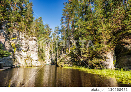 Landscape of Adrspach-Teplice Rocks area, in Hradec Kralove Region in the Czech Republic, Europe. Picturesque river winding through a rocky, tree-lined landscape under a sunny blue sky. 130268481