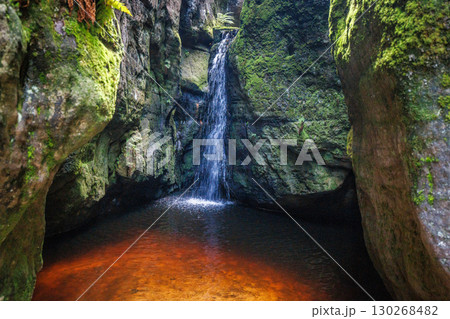 Adrspach-Teplice Rocks, sandstone formations in Hradec Kralove Region in the Czech Republic, Europe. A tranquil waterfall cascades into a pool surrounded by moss-covered rocks in a hidden grotto. 130268482