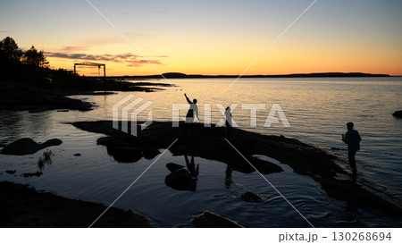 Silhouetted people on rocks against tranquil sunset sky over calm White Sea in Russian Karelia, concept of landscape, travel and nature 130268694