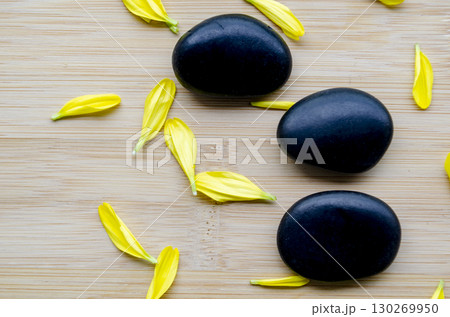 Top view of three black zen stones with scattered yellow petals arranged on wood clean look with customizable space for text 130269950