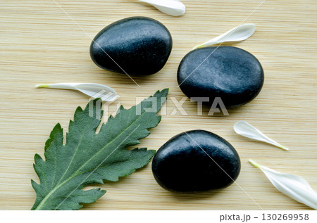 Single green leaf with polished black stones on light wooden base with customizable space for text Single green leaf with polished black stones on light wooden base with customizable space for text 130269958