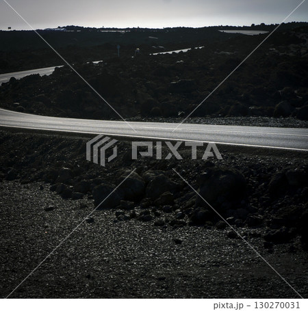 A beautiful asphalt road among black volcanic landscapes with lava formations. 130270031