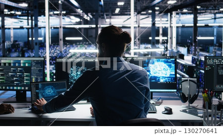 Server room software developer using AI to review infrastructure diagnostics. IT employee in data center analyzing performance data using artificial intelligence technology on devices, camera A 130270641
