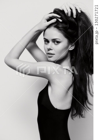 Elegant woman with long dark hair posing in a black bodysuit, showcasing confidence and grace against a textured light background. Fashion and beauty concept. 130271721