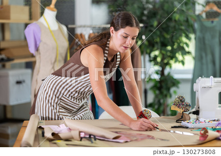Female fashion designer drawing on paper with curved rulers in workshop 130273808