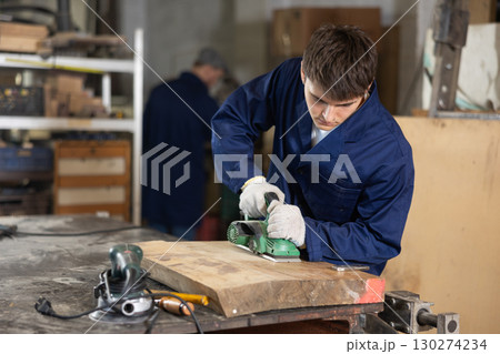 Young guy polishing wooden board in workshop Young guy polishing wooden board in workshop 130274234