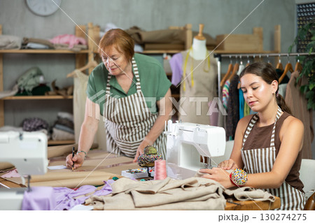 Young woman sewing female assistant drawing pattern on paper 130274275