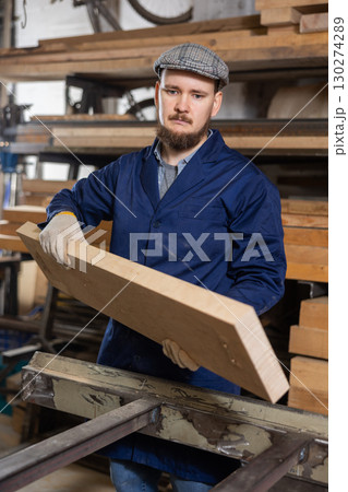 Male worker carries board from storage location to processing location. Selects planks for furniture manufacture 130274289